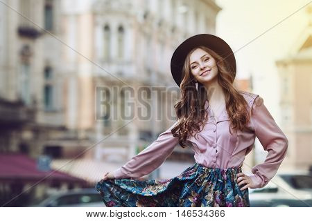 Outdoor portrait of a young beautiful fashionable happy lady posing on a street. Model wearing stylish clothes. Girl looking at camera. Female fashion. City lifestyle. Copy space. Toned.