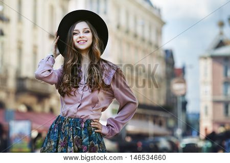 Outdoor portrait of a young beautiful fashionable happy lady posing on a street of the old city. Model wearing stylish clothes. Girl looking at camera. Female fashion. City lifestyle. Copy space.