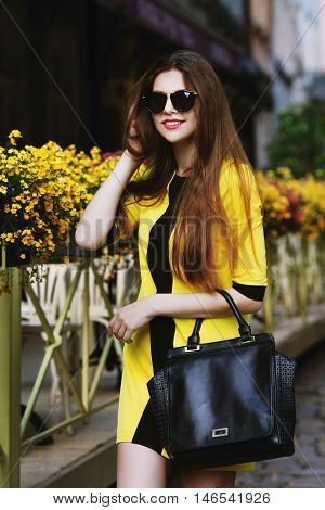 utdoor portrait of young beautiful happy smiling lady walking on street. Model wearing sunglasses and stylish summer dress. Girl looking at camera. Female fashion concept. City lifestyle. Sunny day.