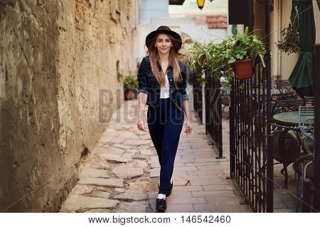 Portrait of young beautiful woman wearing hat walking in the old city. Street fashion concept. Toned.