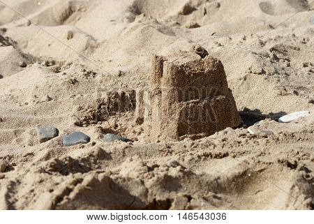 A sandcastle on the beach with some pebbles