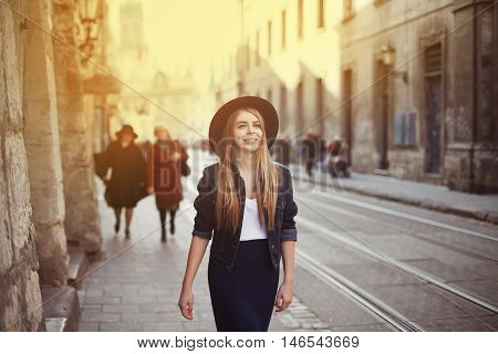 Portrait of young beautiful woman wearing hat walking in the old city. Street fashion concept. Toned.