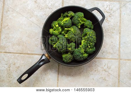 Broccoli in a dark black pan isolated on a stone tile