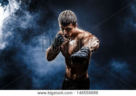 Muscular kick-box or muay thai fighter punching in smoke.