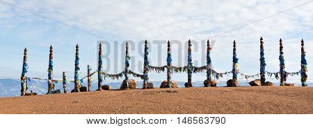 Traditional wooden poles to the hitching post serge. Prayer flags. Buryat tradition on the shores of Lake Baikal in the winter mountains in the background. Winter Landscape on Olkhon island. Buryat Region, Russia, Siberia.