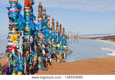 Traditional wooden poles to the hitching post serge. Prayer flags. Buryat tradition on the shores of Lake Baikal in the winter mountains in the background. Winter Landscape on Olkhon island. Buryat Region, Russia, Siberia.