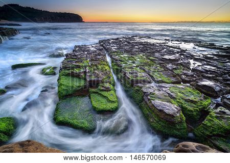 The wave flows over weathered rocks and boulders at Turimetta Beach rock shelf on sunrise. Sydney Australia