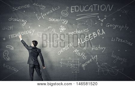 Rear view of man drawing education concept on blackboard with chalk