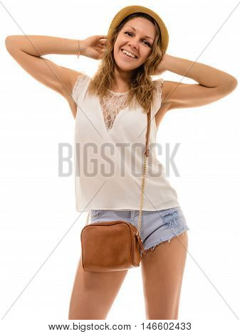 Cheerful young attractive girl in a straw hat and denim shorts with a small bag over his shoulder is holding up his hands behind his head isolated on white.
