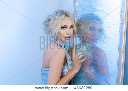 Beautiful young woman in crown and silver top standing near frozen mirror. Snow queen. Copy space.