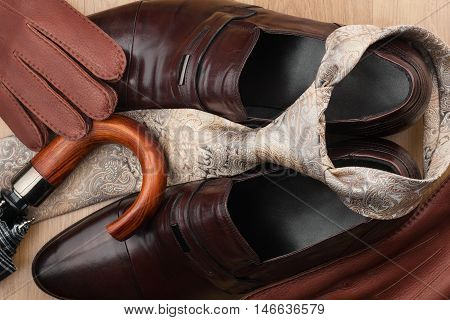 Men's classic accessories: brown shoes tie umbrella and gloves on a wooden surface top view