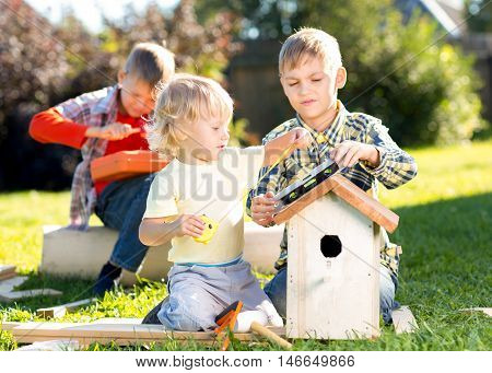 Three little boys brothers building birdhouse outdoors
