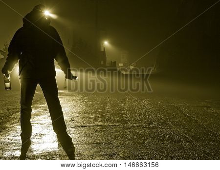 Drunk man silhouette standing in road on foggy night car headlights approaching bottle in hand