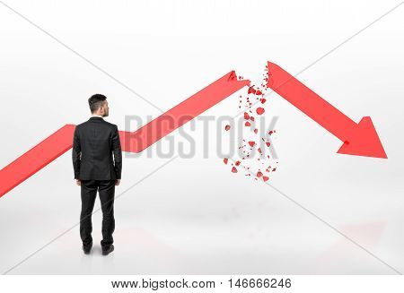 Back view of a businessman looking at red broken arrow of falling graph isolated on white background. Stock market selloff. Economic crisis. Bad luck and problems.