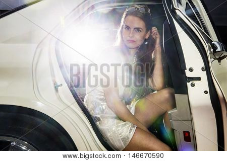 Pretty woman in the door opening of a limousine, ready to get out, and mingle in the nightlife. Bright lights from behind