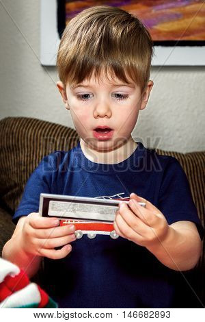 A cute little boy looks at something he has pulled out of his Christmas stocking. His eyes are wide and his mouth is open in surprise.