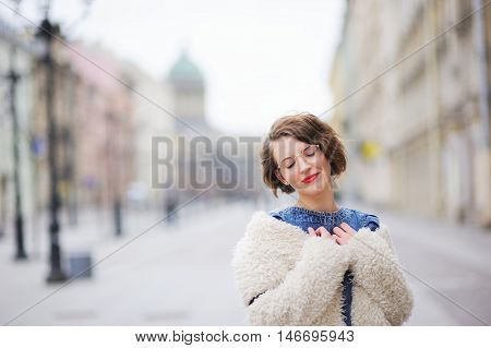 Beautiful young smiling girl posing on the boulevard in the center of St. Petersburg, closing her eyes in embarrassment.