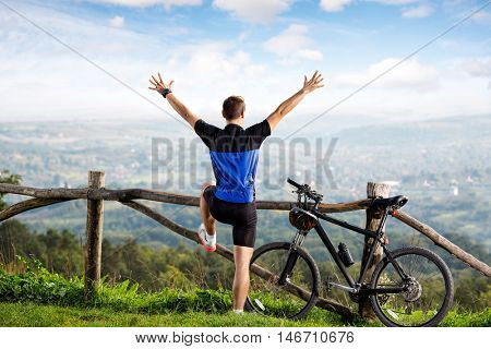 Happy male biker posing with raised hands on a mountain bike outdoor