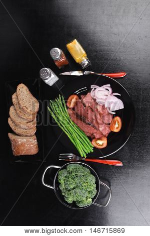 business lunch fresh roast beef meat slices on black plate wotj cutlery asparagus boiled broccoli rye bun on wooden table