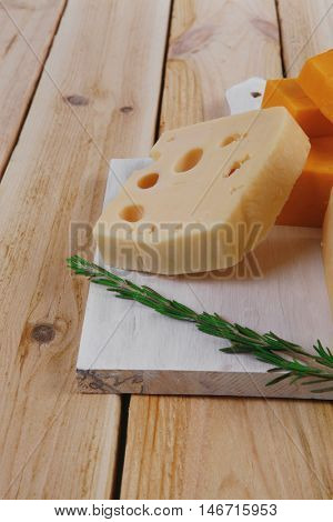 various types of fresh raw aged delicatessen cheese on white plate over light wooden table cheddar swiss