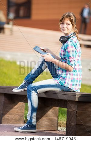 Preparing to exams outdoors. Beautiful young female student writing or reading something from note pad.  Woman sitting on bench in city park.