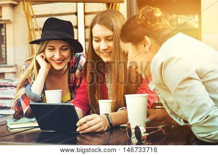 Group of girls sits in coffee house with tablet computer and having fun