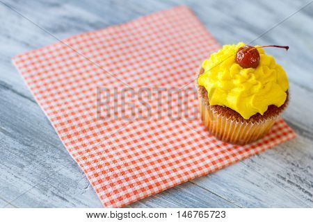 Yellow cupcake on a napkin. Red cherry on icing. Dessert served at the diner. How to lift mood.
