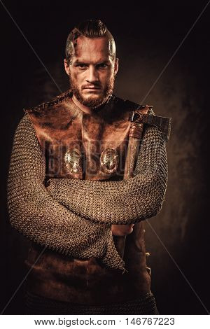 Serious viking in a traditional warrior clothes, posing on a dark background.