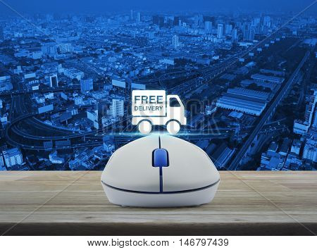 Wireless computer mouse with free delivery truck icon on wooden table over city tower street and expressway Transportation business concept