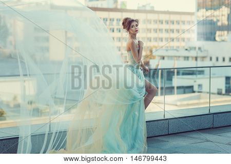 Young girl standing on the balcony her dress fluttering in the wind.