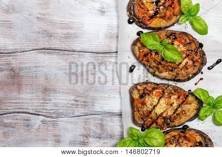 Baked eggplant stuffed with vegetables and cheese with addition aromatic herbs and sauce on paper. Delicious vegetarian dish. top view, sopy space