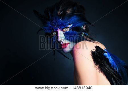 Halloween Makeup. Fantasy Bird Woman with Artistic Make-up on Blue Background and Copy space for Text