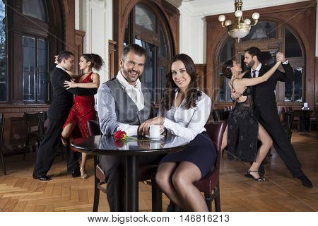 Smiling Couple Sitting At Table While Dancers Performing Tango