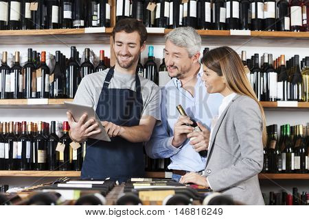 Salesman Showing Wine Information To Couple On Digital Tablet