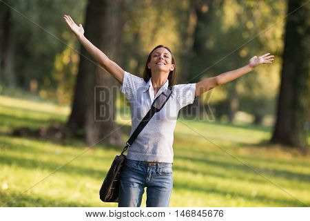 Beautiful businesswoman enjoys in the park with her arms outstreched.