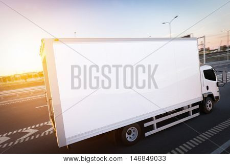 Commercial cargo delivery truck with blank white trailer driving on highway. Generic, brandless vehicle design. 3D rendering