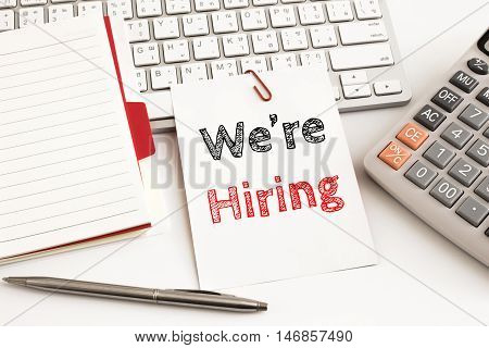 Word text We're hiring on white paper card on office table / business concept