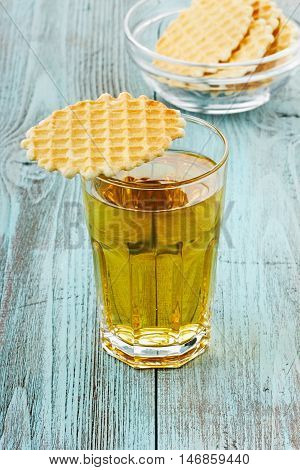 Apple juice in a glass with wafer cookies on a wooden surface.