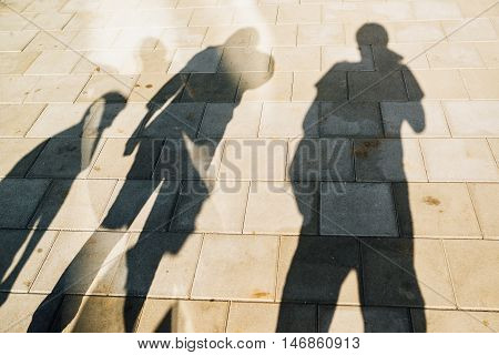 People casting shadows on the pavement four young man and women overshadowing street concrete tiles