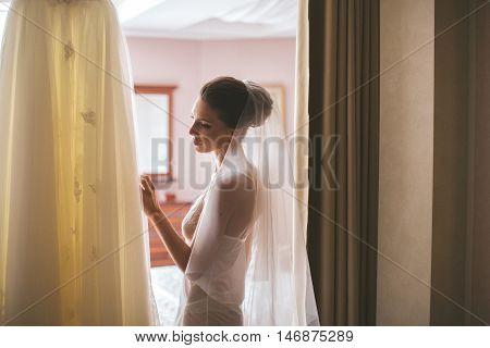 Fiancee stands in underclothes and touches wedding dress