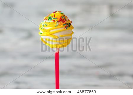 Cake on stick. Sprinkles and yellow icing. Sugar is the main ingredient. Small wonder of cooking.