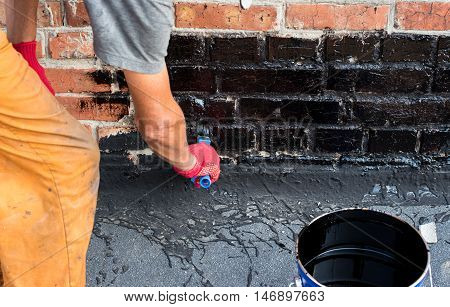 Roofer covered brick wall bitumen primer for improving adhesion during surfacing contiguity with rolled waterproofing during the installation of flat roof.