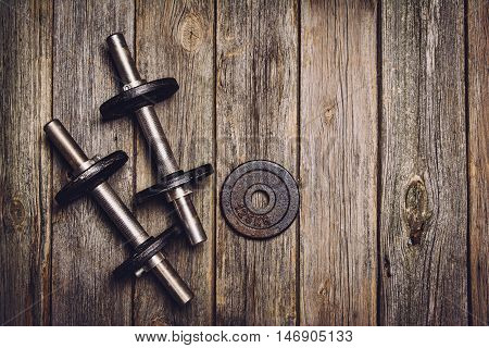 Old iron dumbbells or exercise weights with extra plates on an old wooden deck, floor or table. Image taken from above, top view. A lot of copy space around product