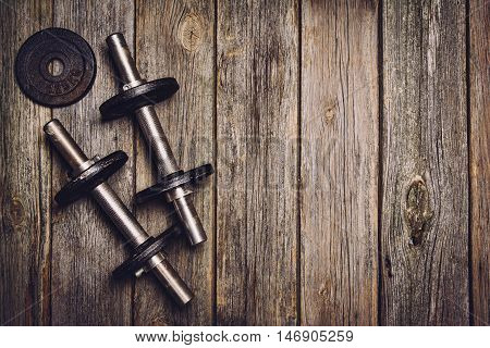 Old iron dumbbells or exercise weights with extra plates on an old wooden deck, floor or table. Image taken from above, top view. A lot of copy space around product