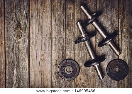 Old iron dumbbells or exercise weights with extra plates on an old wooden deck, floor or table. Image taken from above, top view. A lot of copy space around product