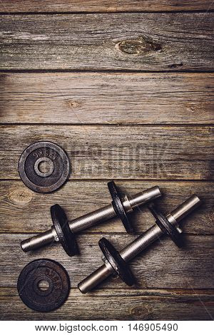 Old iron dumbbells or exercise weights with extra plates on an old wooden deck, floor or table. Image taken from above, top view. A lot of copy space around product