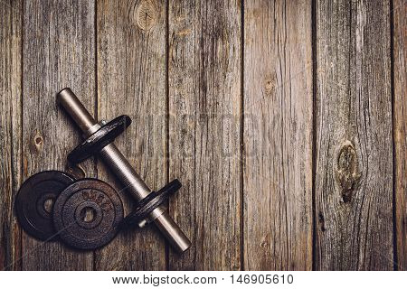 Old iron dumbbells or exercise weights with extra plates on an old wooden deck, floor or table. Image taken from above, top view. A lot of copy space around product