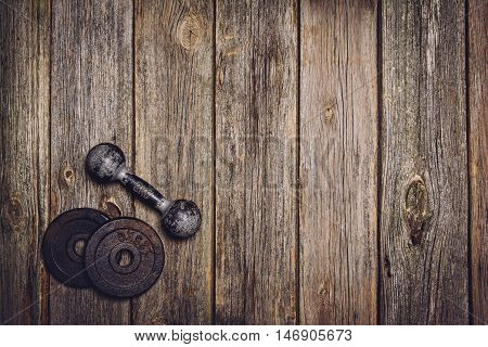 Old iron dumbbells or exercise weights with extra plates on an old wooden deck, floor or table. Image taken from above, top view. A lot of copy space around product
