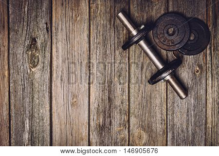 Old iron dumbbells or exercise weights with extra plates on an old wooden deck, floor or table. Image taken from above, top view. A lot of copy space around product