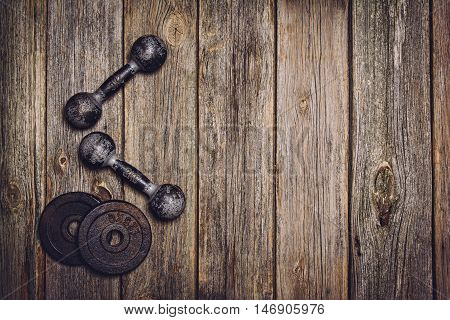 Old iron dumbbells or exercise weights with extra plates on an old wooden deck, floor or table. Image taken from above, top view. A lot of copy space around product
